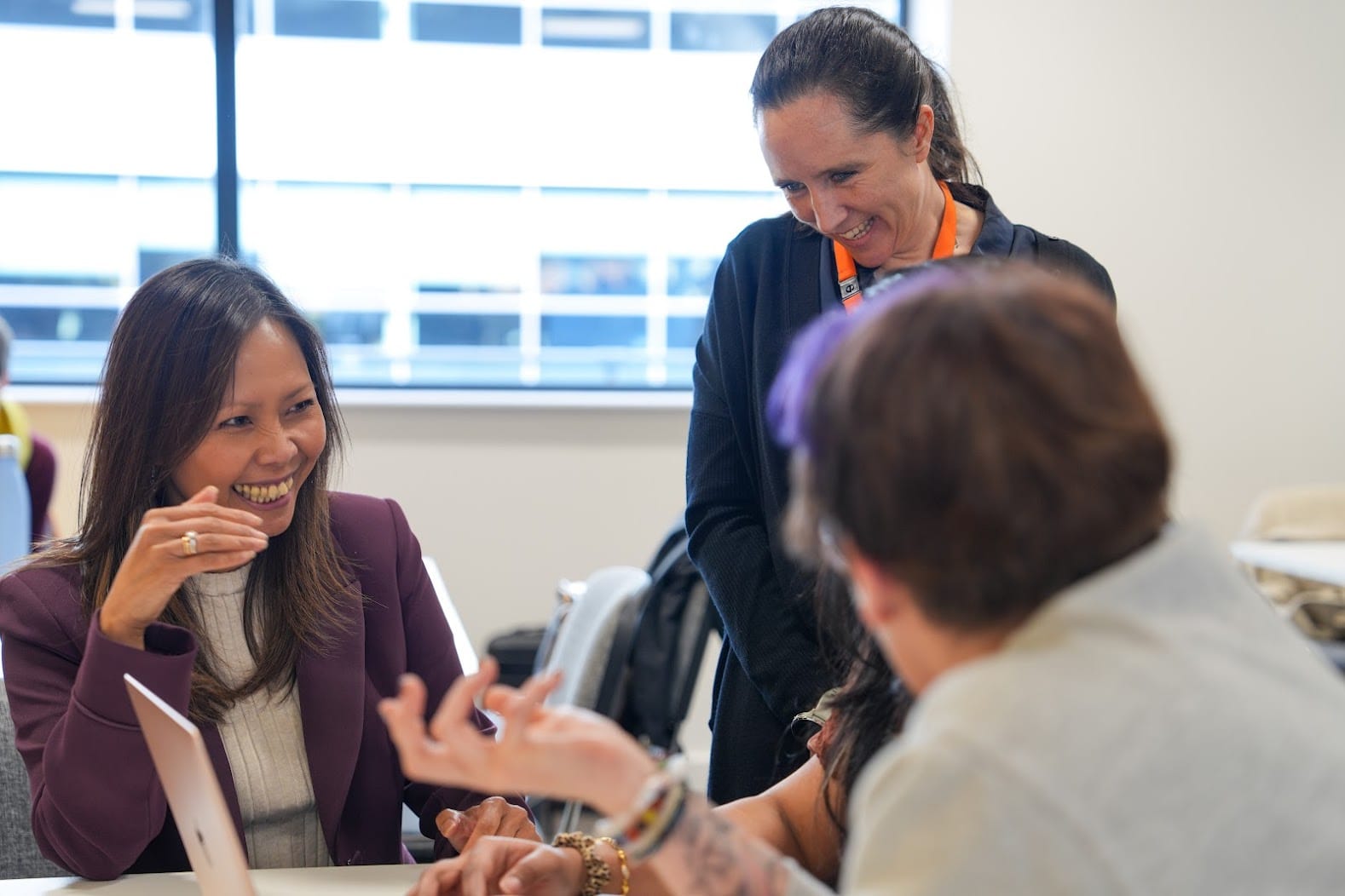 Two women smiling while speaking to a group in a professional setting.