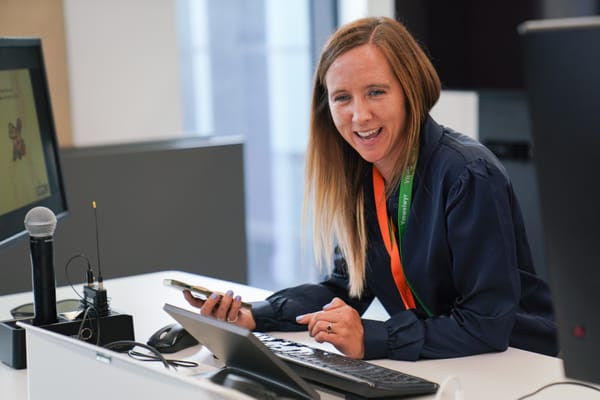 Photo of a white lady at a desk laughing, holding a phone.