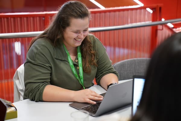 Woman in a professional building, smiling down at her laptop. 